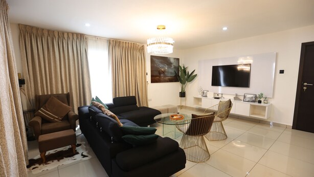 A modern living room with a sofa set, a glass coffee table, and a TV mounted on the wall.