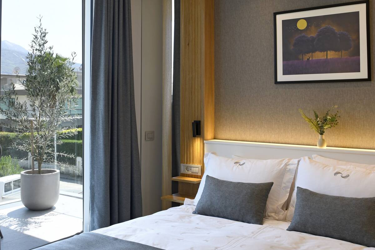 Quarto de hotel com cama grande, mesa de cabeceira, planta em vaso e pintura na parede.