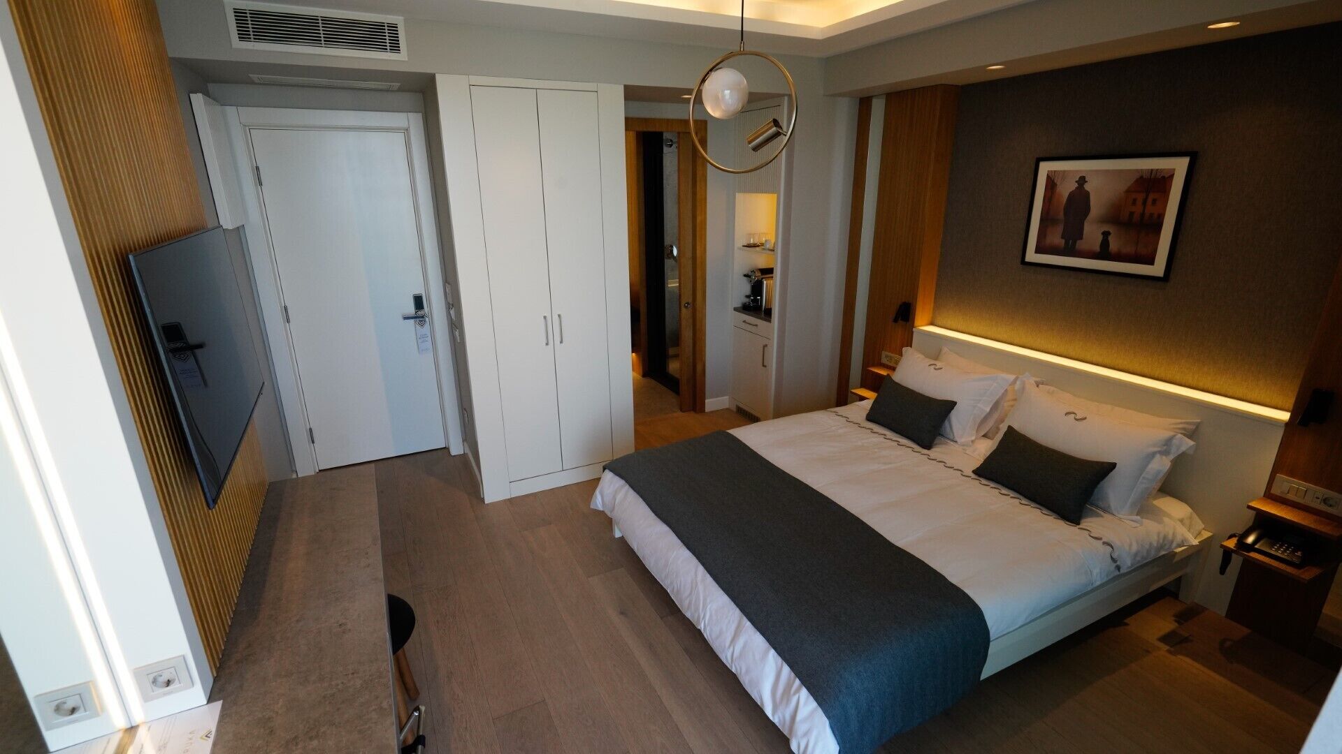 Quarto de hotel com uma cama grande, televisão, guarda-roupa e um quadro na parede.