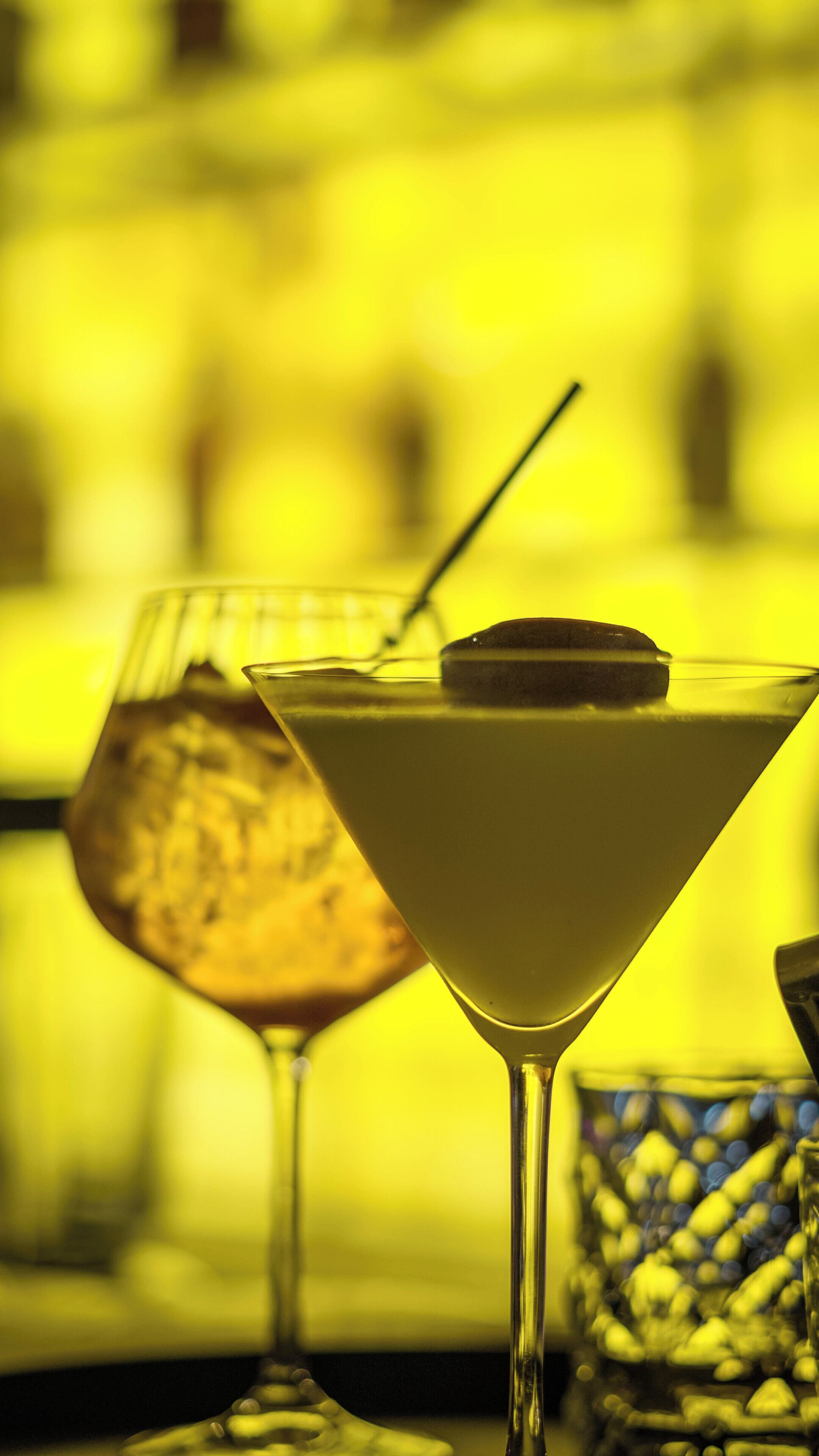 Un verre à martini, garni d’une tranche de citron et muni d’une paille, posé sur une table devant un arrière-plan flou.