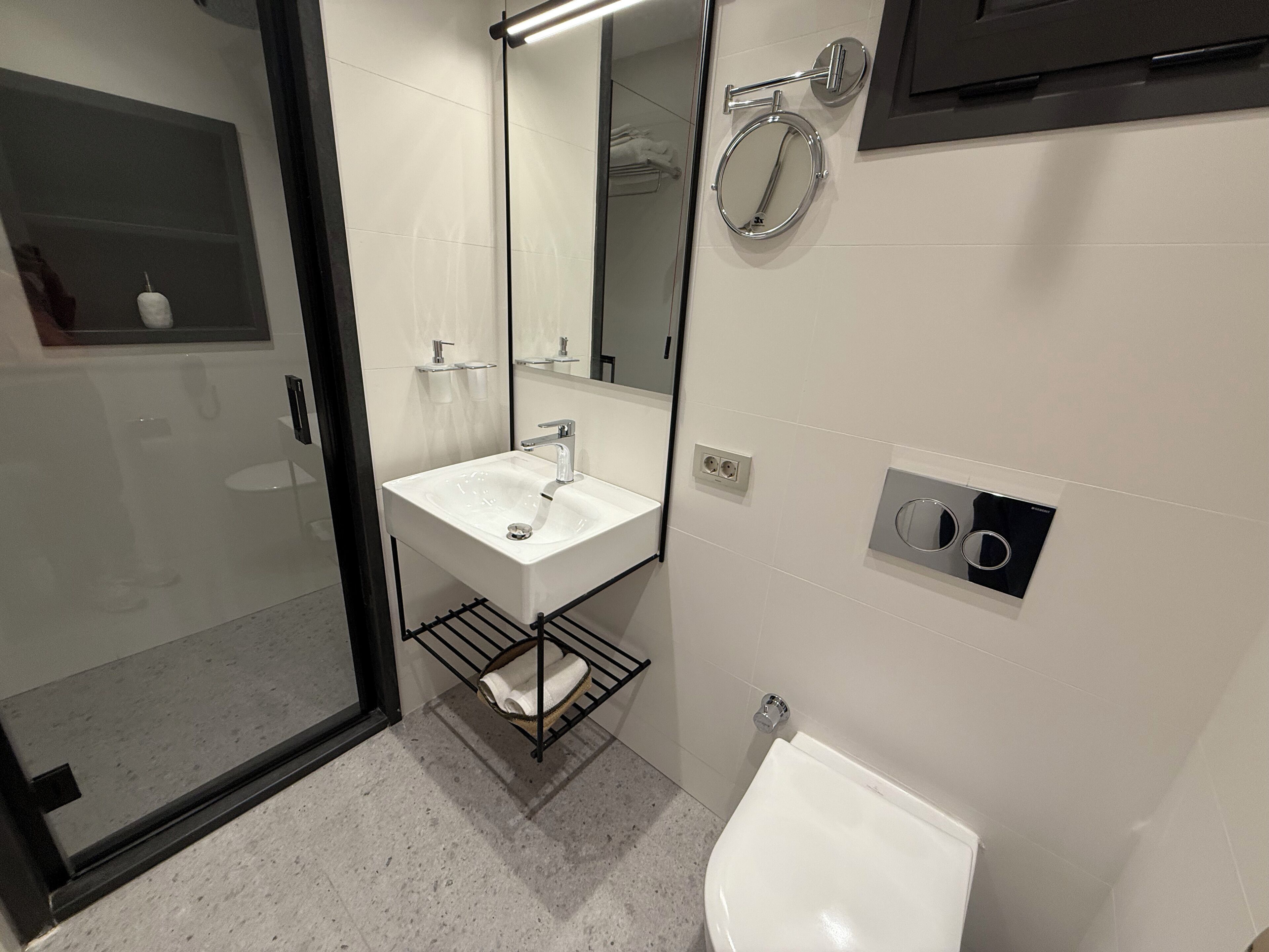 A modern bathroom with a glass shower enclosure, a white sink with a mirror above, a towel rack, and a toilet.