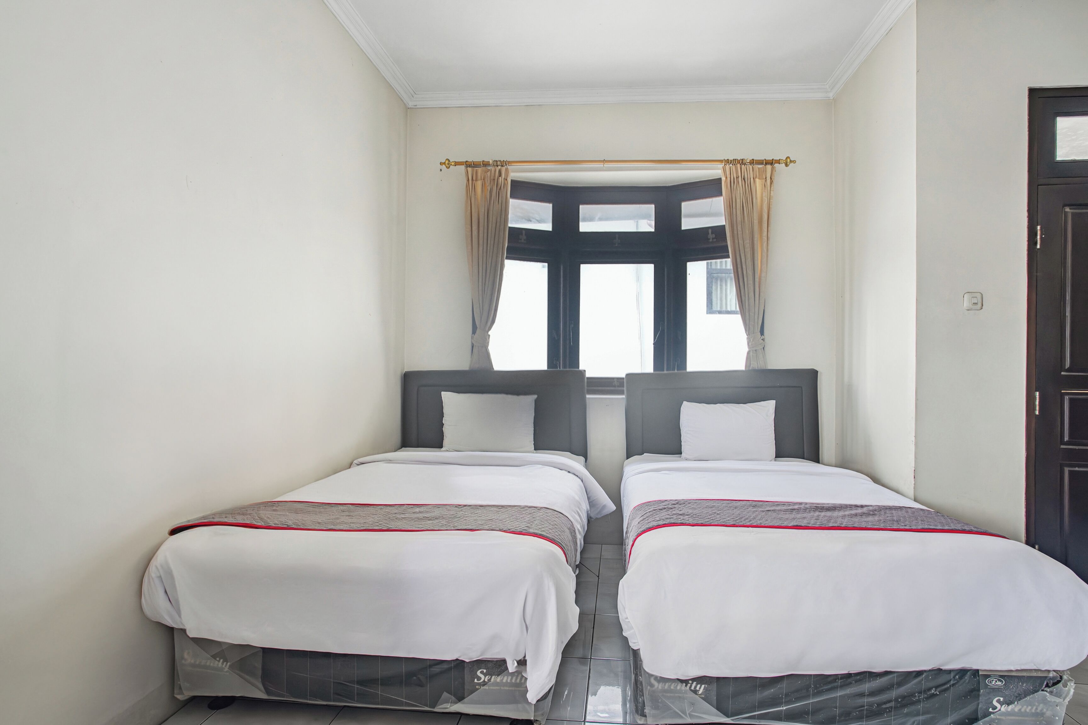 A double room with two beds, a window with curtains, and a door.
