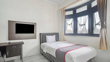 A bedroom with a bed, a desk, a television mounted on the wall, and a window with curtains.