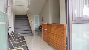 Ein Empfangsbereich mit einem Holztisch, eine Wartezone mit Sesseln und eine Treppe, die zu einer oberen Etage führt.