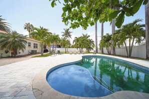 A swimming pool with a curved edge, surrounded by a paved patio area with lounge chairs and palm trees. - Hollywood Beach | Sleeps 10 Modern Beach Villa (Hollywood)