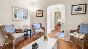 Una sala de estar acogedora con sillones de mimbre, una mesa de centro blanca y cuadros en las paredes.