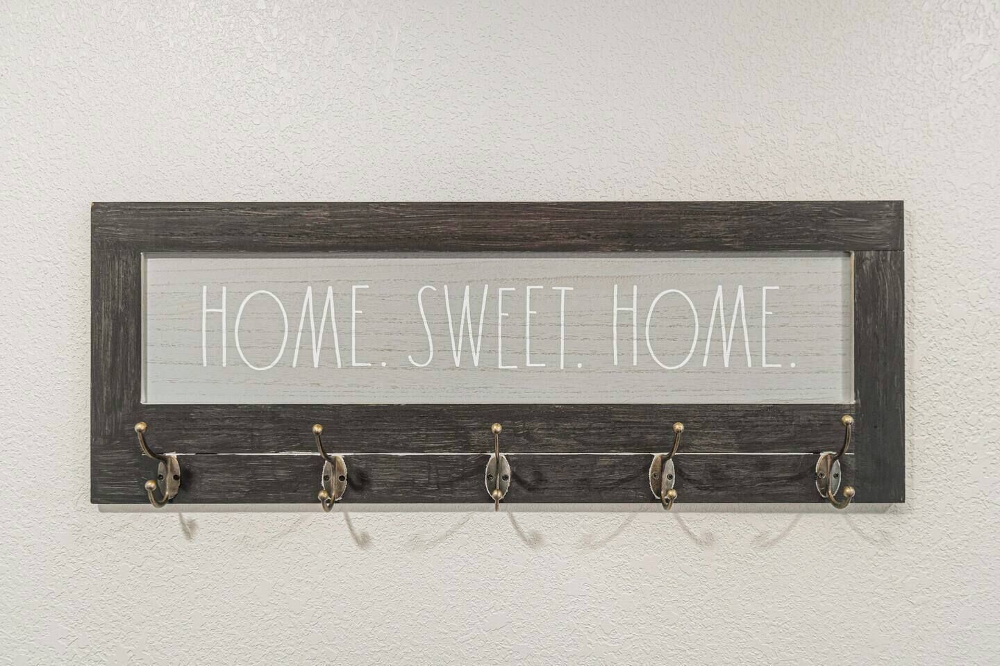 A wall-mounted sign with the text "HOME. SWEET. HOME." and five hooks below it.