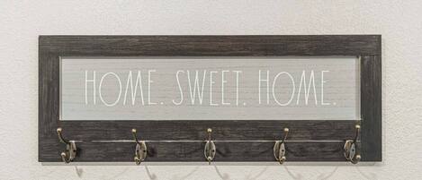 A wall-mounted sign with the text "HOME. SWEET. HOME." and five hooks below it.