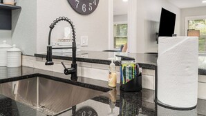 A modern kitchen with a stainless steel sink, black faucet, and a black soap dispenser. There is a paper towel holder and a clock on the wall. - 12m to Belton<br>Outdoor dining<br>Long Stays welcome<br>Huge fully stocked kitchen<br>Master Suite<br>On-site laundry<br>Utilities included<br>Fuller furnished<br>Natural light<br>Block out shades (Grandview)