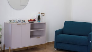 A room with a light purple cabinet, a blue sofa, and a round mirror on the wall.