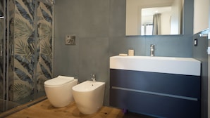 A modern bathroom with a shower enclosure, a toilet, a bidet, and a sink with a mirror above it.