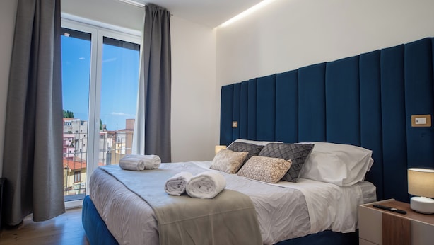 A modern hotel room with a large bed, a view of the city, and a nightstand with a lamp.