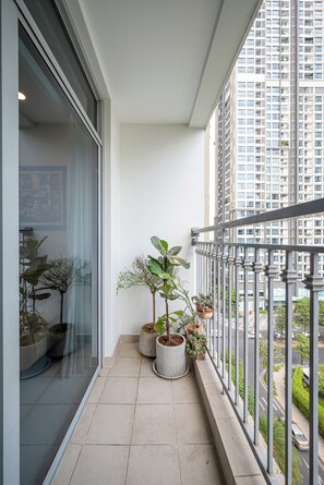 A balcony with potted plants, a view of a tall building, and a tiled floor.