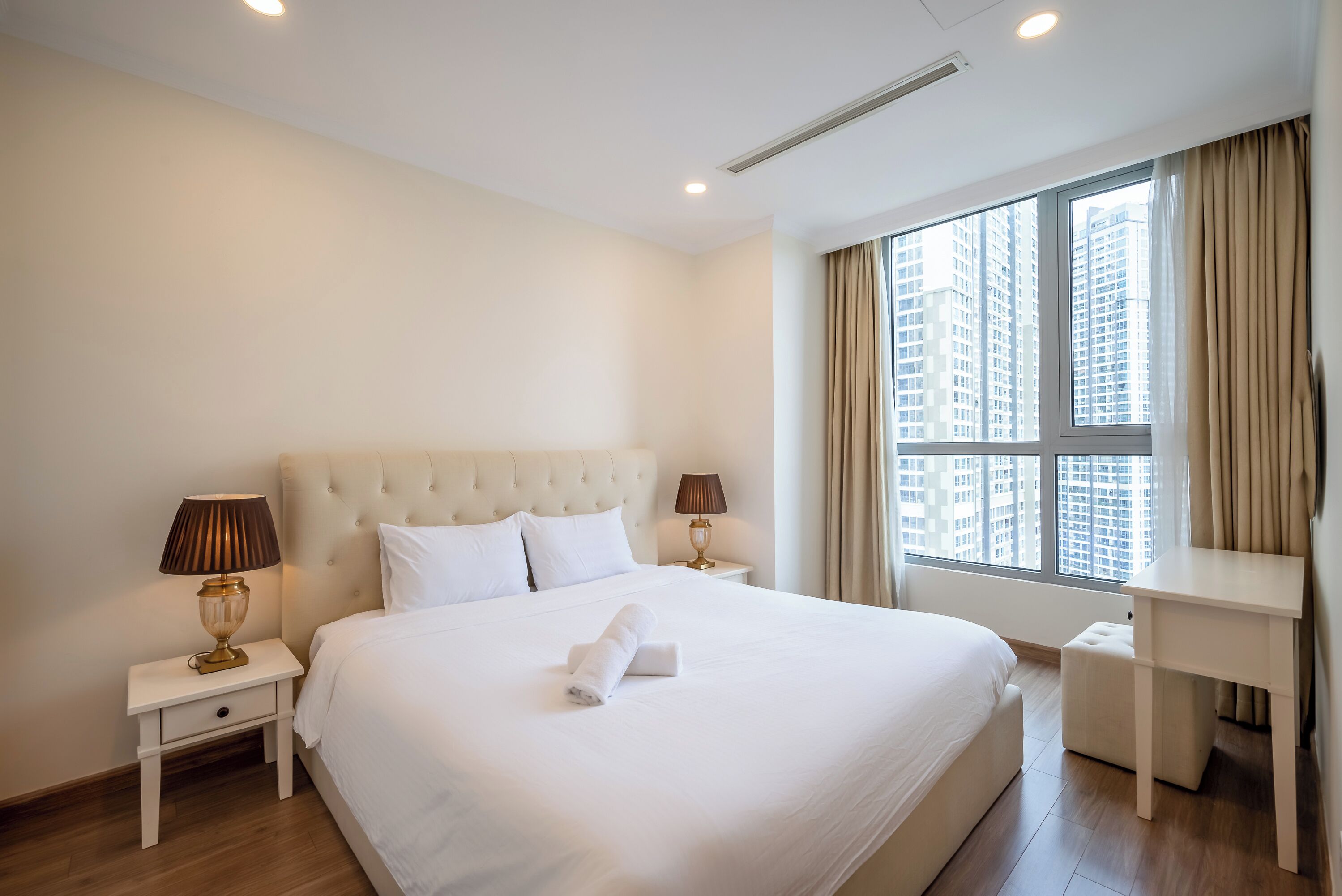 A hotel room with a large bed, two bedside tables, a desk, and a window with curtains.