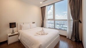 A hotel room with a large bed, a bedside table with a lamp, and a view of a cityscape through a large window. - PD Pristine Apartment Landmark Plus (Ho Chi Minh City)