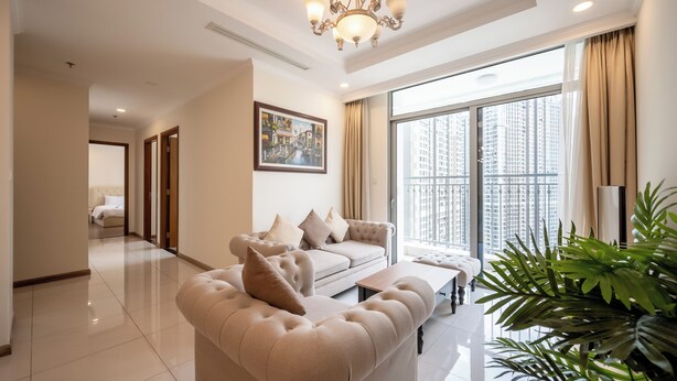 A spacious living room with a beige sofa, a coffee table, and a large window offering a city view. - PD Pristine Apartment Landmark Plus (Ho Chi Minh City)