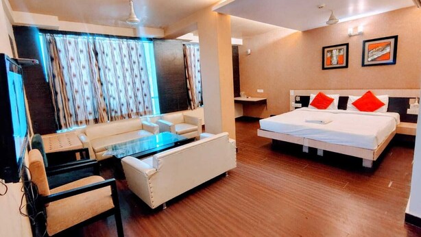 A modern hotel room with a sofa, a bed with red pillows, a glass coffee table, and a TV. - Hotel Apex Intercontinental (Jaipur)