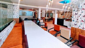 A modern restaurant with long communal tables, individual booths, and a bar area. - Hotel Apex Intercontinental (Jaipur)