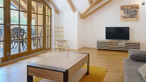 A spacious living area with a large sliding glass door, a wooden coffee table, a TV on a wooden stand, and a striped sofa. - Beautiful apartment for 4 guests with pool, WIFI, TV and terrace (Rauris)