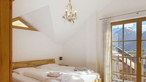 A bedroom with a wooden bed, a chandelier, a nightstand, and a view of mountains through large windows. - Beautiful apartment for 4 guests with WIFI, pool, TV and terrace (Rauris)