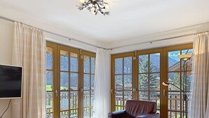 A spacious living room with a large window, a leather sofa, a wooden coffee table, and a television. - Nice apartment for 6 people with WIFI, pool, TV and terrace (Rauris)