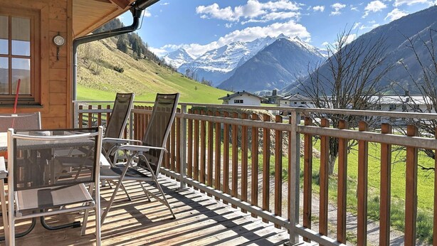 A wooden deck with chairs and a table, overlooking a mountain landscape with houses and a clear sky. - Nice apartment for 6 people with WIFI, pool, TV and terrace (Rauris)