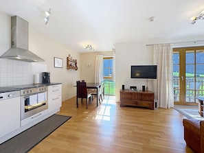 Cozinha moderna com fogão, forno e micro-ondas embutidos. Possui área de jantar com mesa e cadeiras, e uma TV fixada em um armário de madeira.