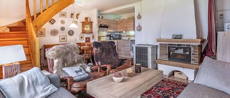 Un salon chaleureux avec un escalier en bois, une cheminée et un coin repas comprenant une table et des chaises.