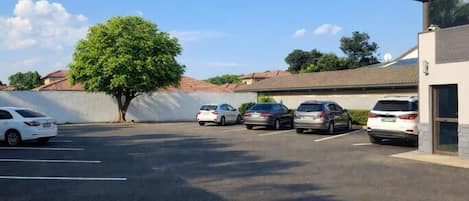 A parking lot with several cars, a building with a flat roof, and a tree in the background.
