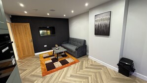 Una sala moderna con un sofá gris, una mesita de centro pequeña y un suelo con patrón de espiga.