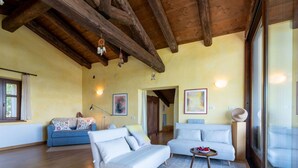 A spacious living room with wooden beams, two sofas, a coffee table, and a large window. - Nice apartment for 4 guests with WIFI, terrace, pets allowed and panoramic view (Igliano)