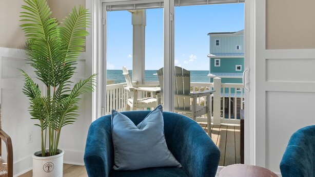 A balcony with a potted plant, a blue chair, and a view of the ocean and buildings.