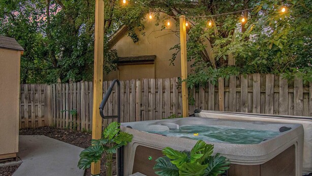 A hot tub with steps, surrounded by a wooden fence, and string lights above. - Warm & Spacious 4BR Retreat w/ Hot Tub & Grill! (Omaha)