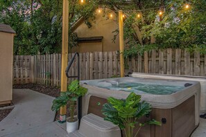 A hot tub with steps, surrounded by a wooden fence, and string lights above. - Warm & Spacious 4BR Retreat w/ Hot Tub & Grill! (Omaha)