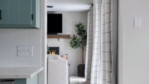 A narrow hallway with a white brick fireplace, a plant, and a curtain. - Warm & Spacious 4BR Retreat w/ Hot Tub & Grill! (Omaha)