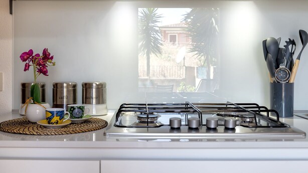 Une cuisine moderne équipée d’une cuisinière à gaz, d’appareils électroménagers en acier inoxydable et offrant une vue sur un quartier résidentiel.