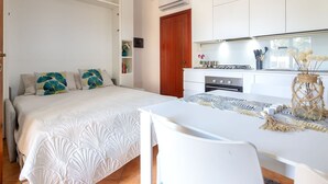 Une chambre comprenant un lit, des tables de chevet, un bureau et un coin cuisine.