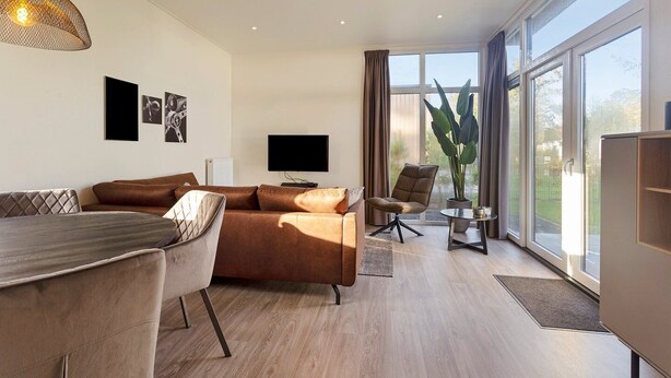 Een moderne woonkamer met een bank, een eettafel, een televisie en een groot raam met gordijnen.