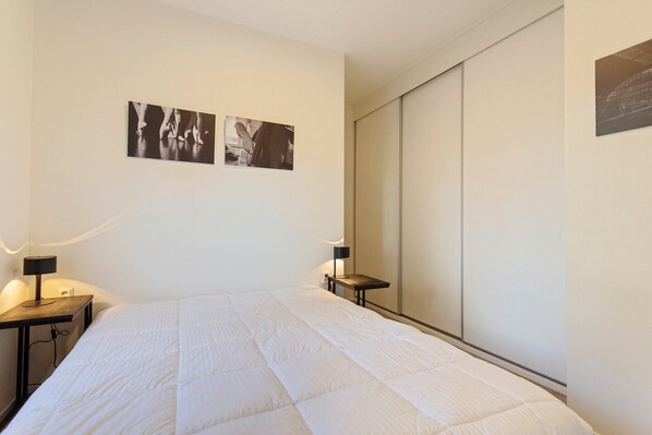 Une chambre d’hôtel avec un grand lit, deux tables de chevet avec des lampes, une armoire et deux photographies en noir et blanc accrochées au mur.