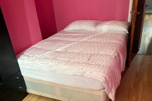 Uma cama de solteiro com colcha estampada em um quarto com paredes cor-de-rosa e piso de madeira.