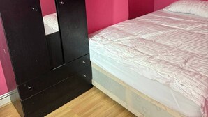 A bedroom with a bed, a wooden floor, and a black wardrobe against pink walls. - 6 Guests - 3 Bedrooms - Close to London Center (London)