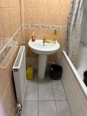 A bathroom with a white sink, a yellow bottle, a black bucket, and a radiator.