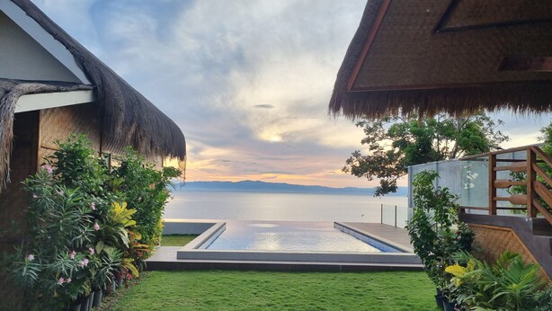 A pool area with a view of the sea, surrounded by potted plants and a thatched-roof structure. - The CLiffhouse Samboan (Samboan)