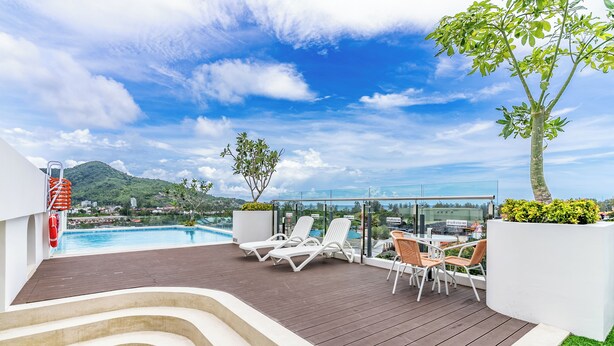 A rooftop pool area with lounge chairs, a glass balustrade, and a view of a mountain and cityscape.