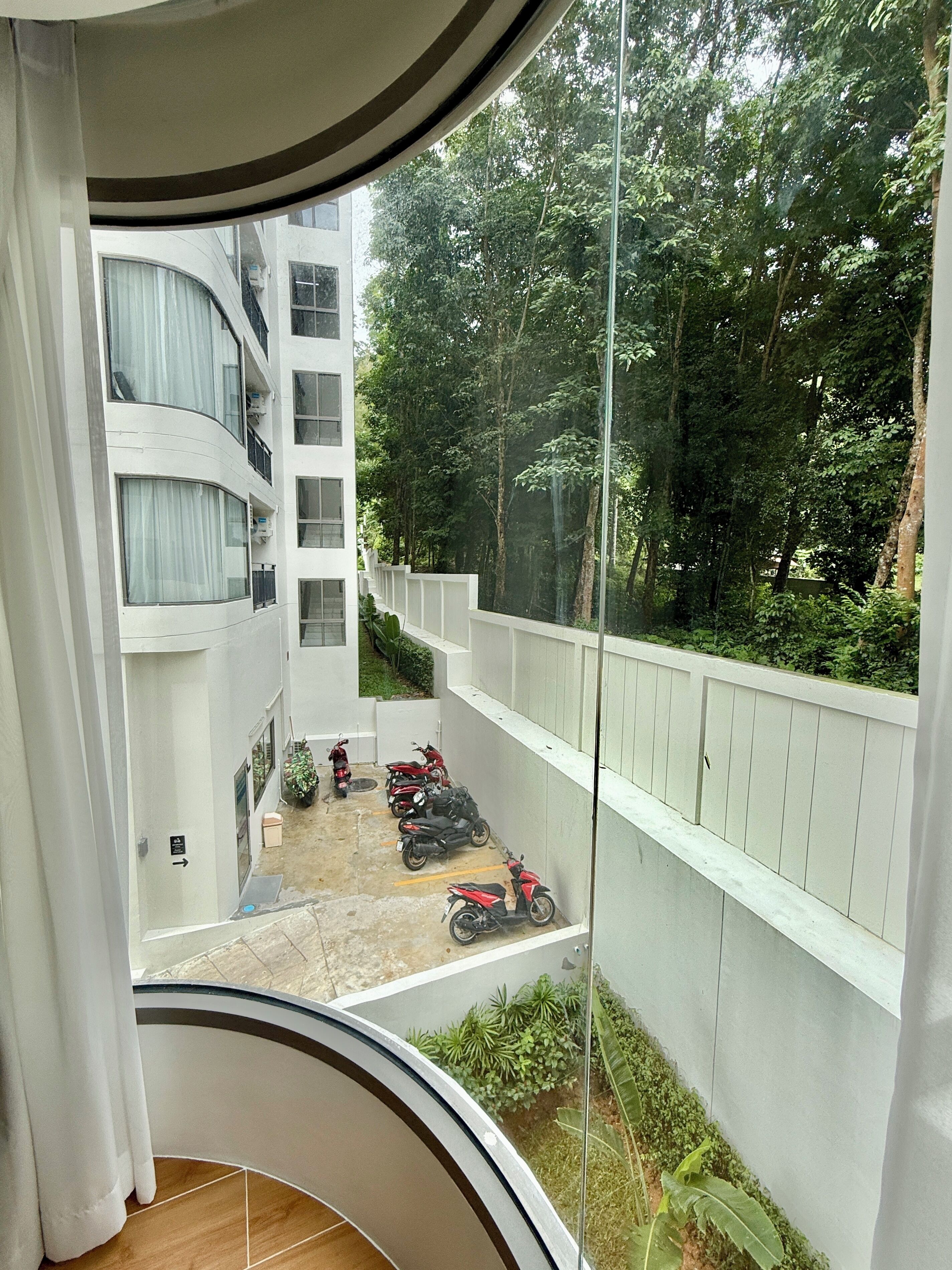 A view from a balcony overlooking a courtyard with parked scooters and a white building with multiple floors and balconies.