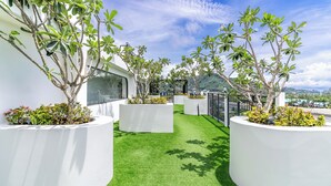 A rooftop garden with artificial grass, white planters, and various shrubs.