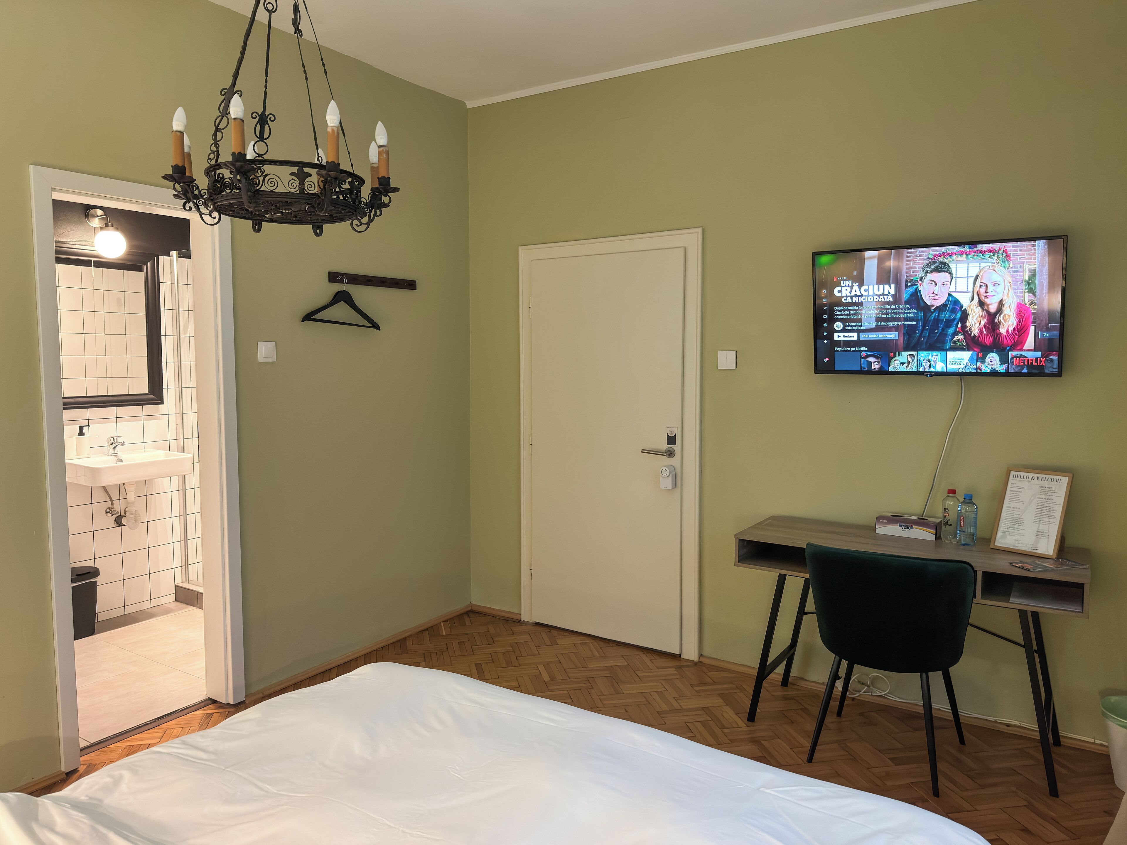 A bedroom with a bed, a desk with a chair, a TV, and a hanging light fixture.
