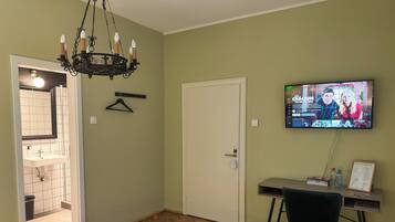 A bedroom with a bed, a desk with a chair, a TV, and a hanging light fixture.