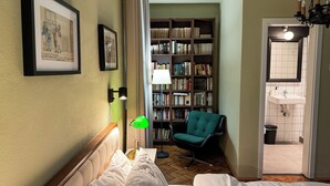 A hotel room with a bed, a green chair, a bookshelf, and a bathroom visible through an open door. - Kesletz House (Sibiu)