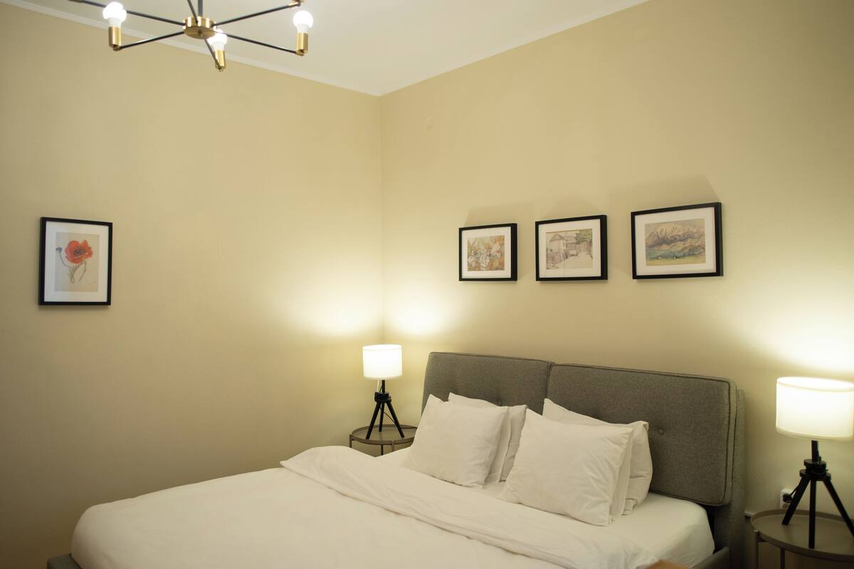 A hotel room with a large bed, a ceiling light fixture, and three framed pictures on the wall.